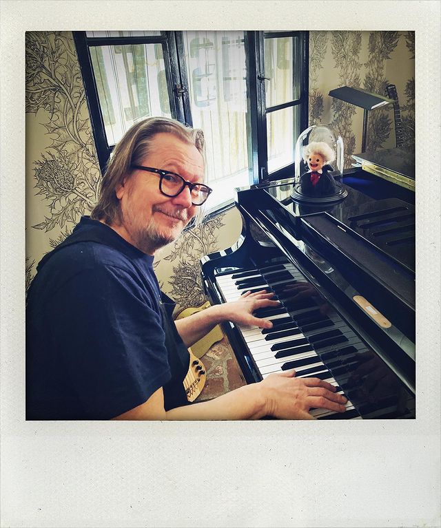 Gary Leonardo Oldman in a noir t-shirt playing the piano.